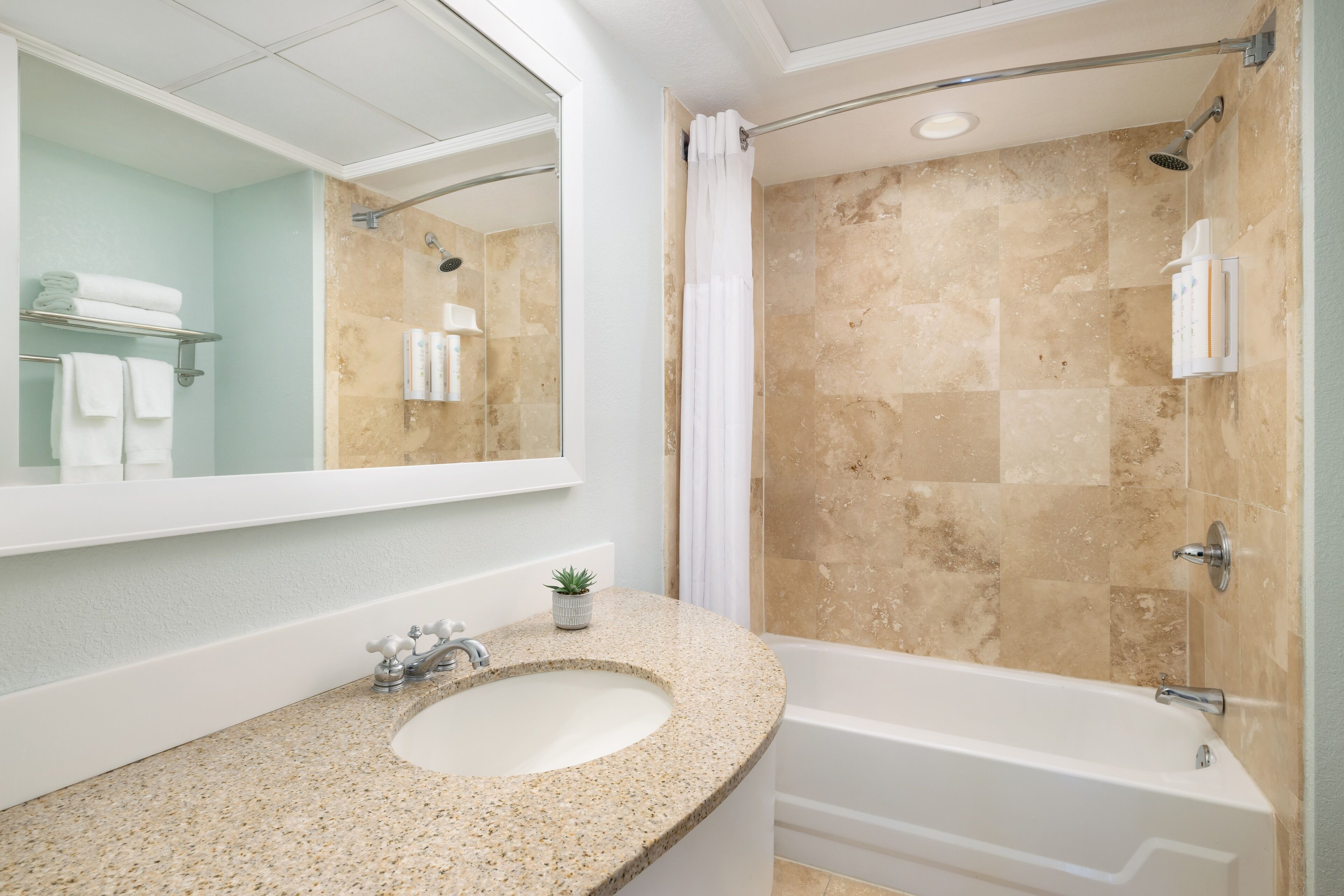 Baño con lavamanos de encimera de granito, espejo grande, ducha con azulejos color beige y bañera blanca.