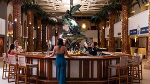 A bar area with a central statue, palm trees, and wooden chairs.