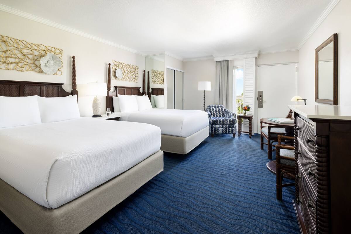 A hotel room with two beds, a desk, a chair, a dresser, and a mirror.