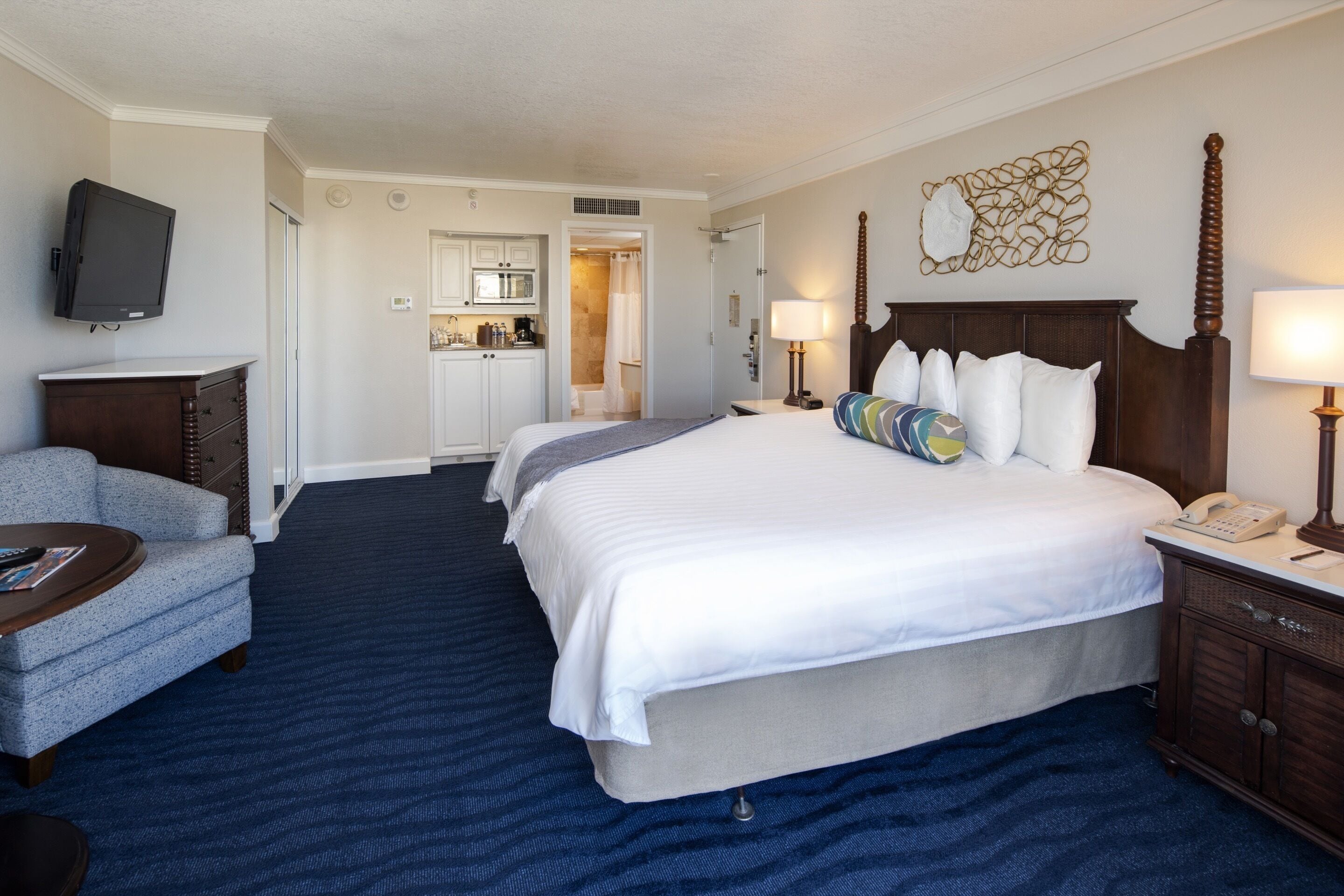 A hotel room with a large bed, a desk, a TV, a kitchenette, and a bathroom.