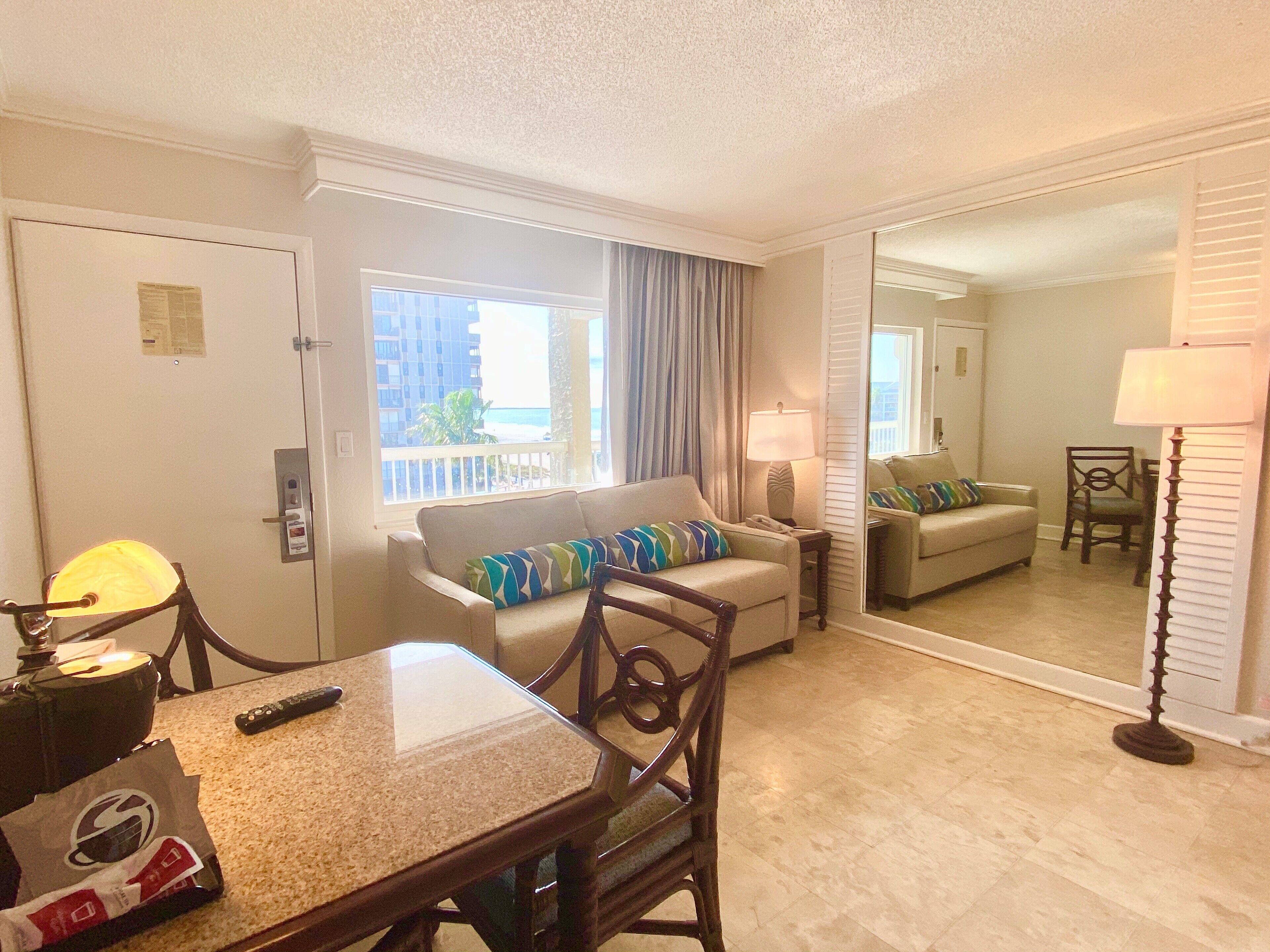 A hotel room with a dining table, two sofas, a mirror, and a view of the ocean.