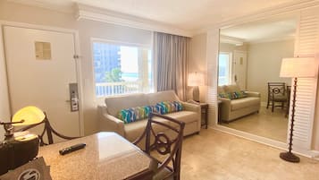 A hotel room with a dining table, two sofas, a mirror, and a view of the ocean.
