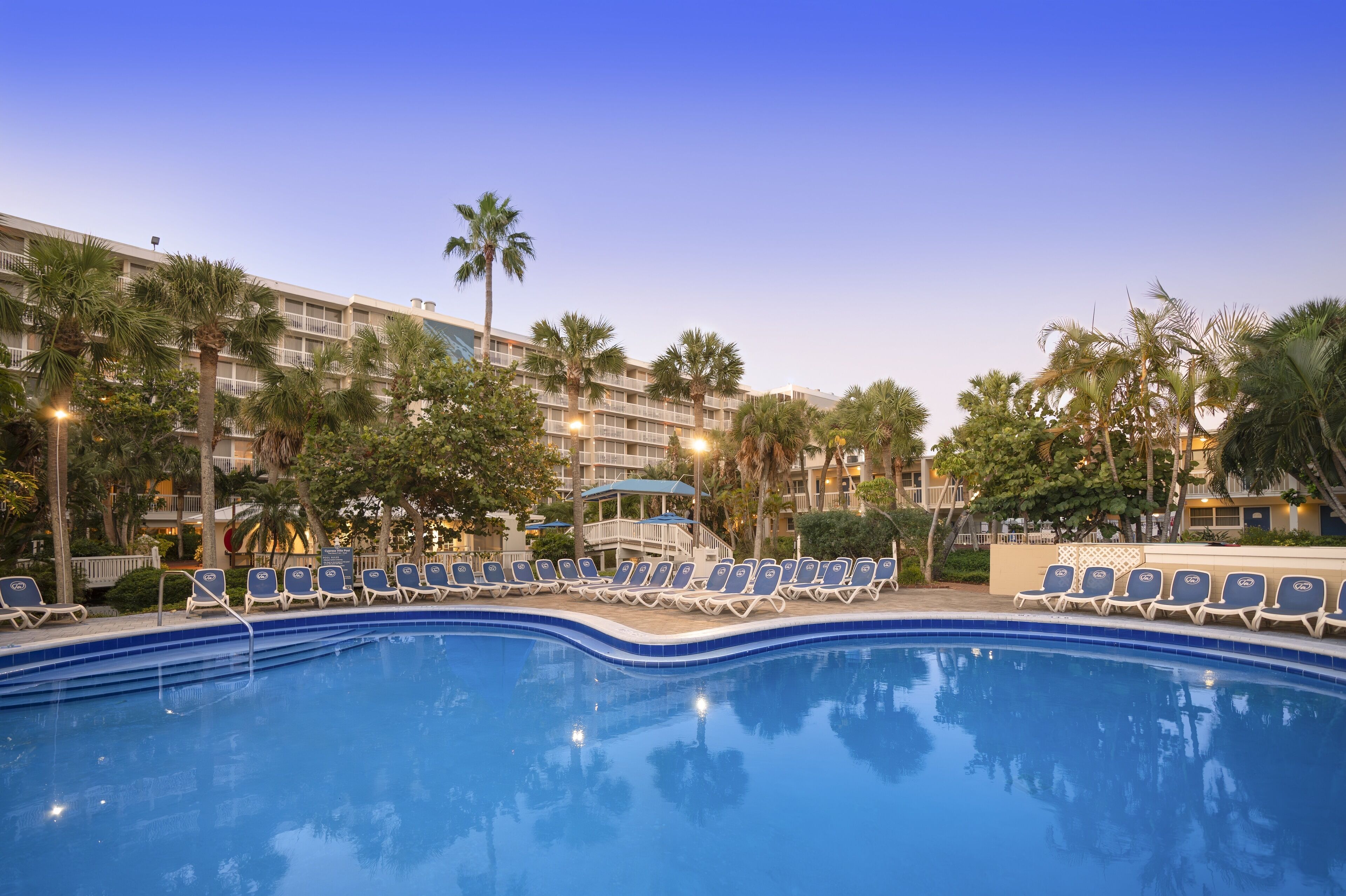A hotel pool area with lounge chairs and palm trees.