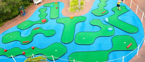 A miniature golf course with multiple green putting areas and a brick pathway.
