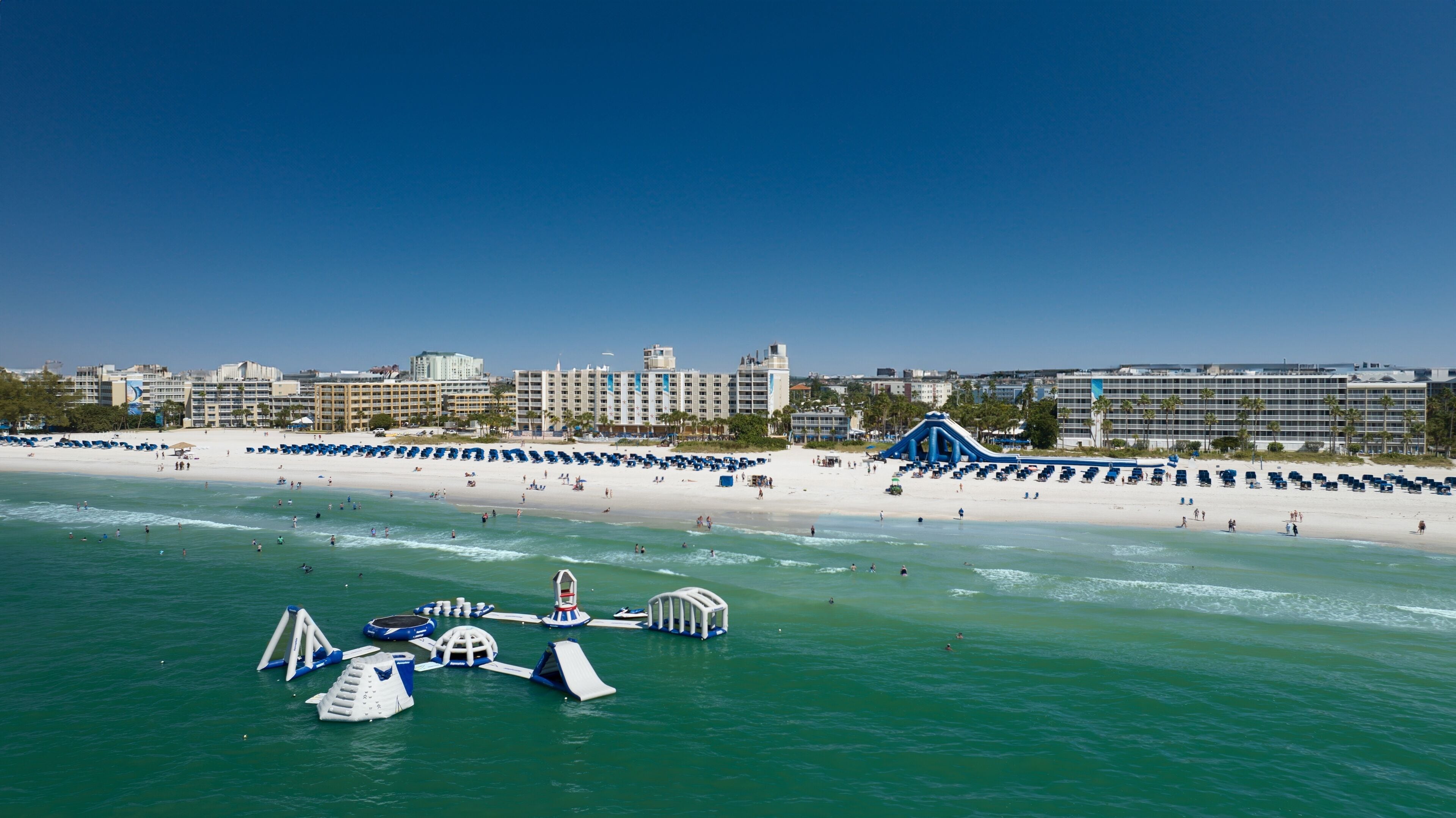 A beach with a water park, including slides and play structures, and a hotel complex in the background.