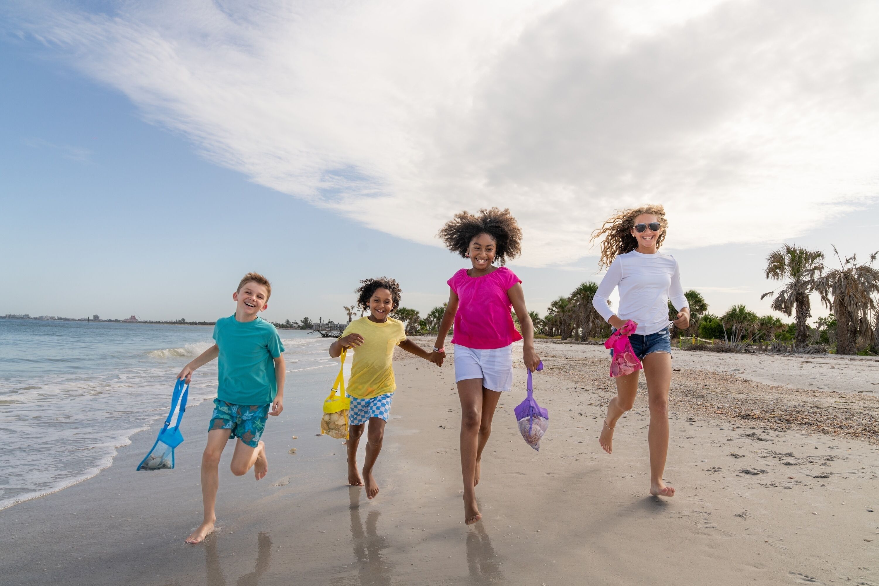 Cuatro personas corriendo en la playa, con el océano y palmeras al fondo.