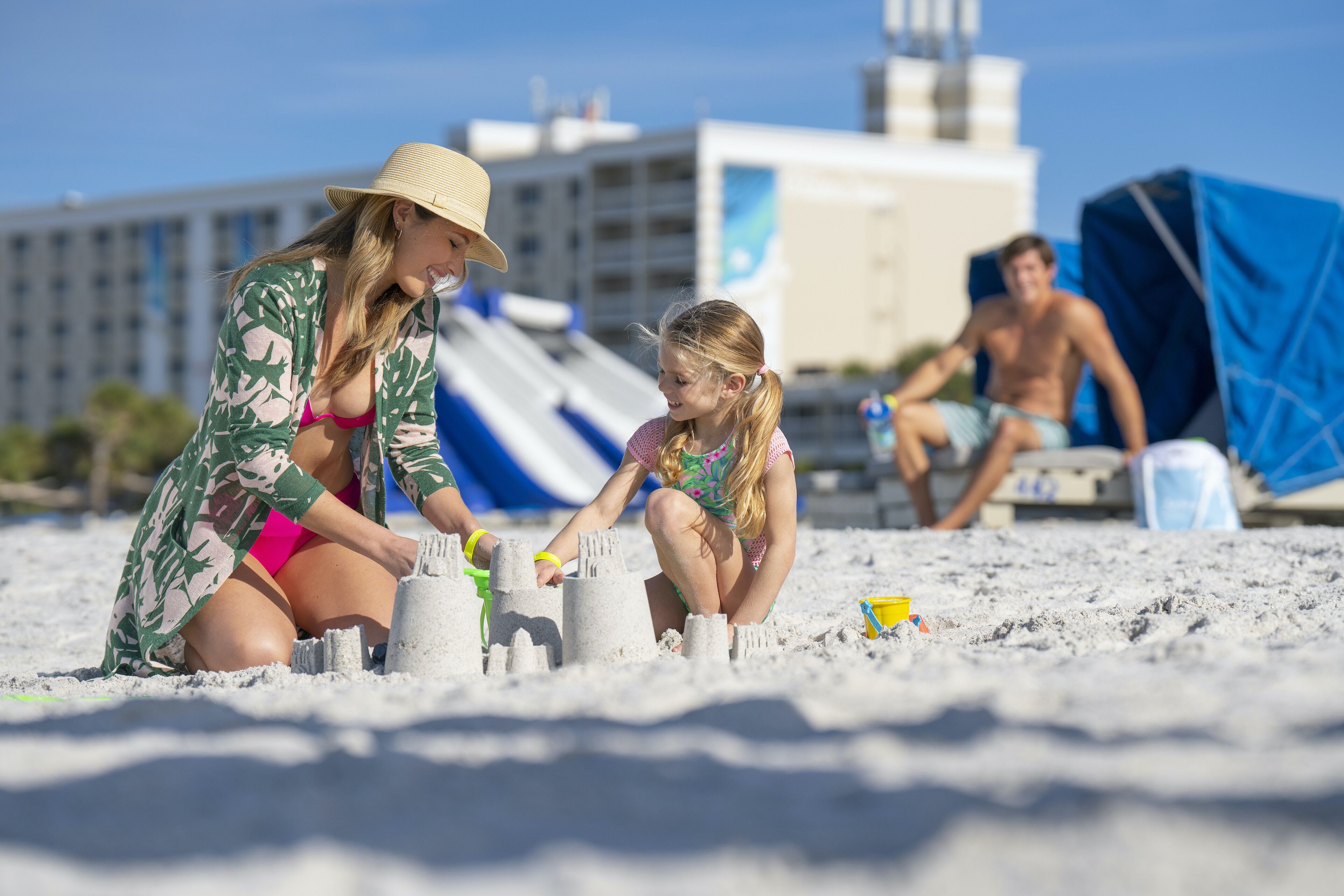 Escena de playa con gente construyendo castillos de arena.