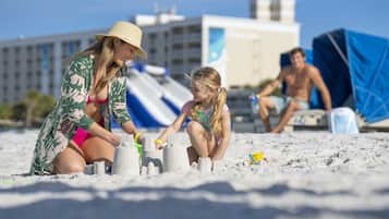 Escena de playa con gente construyendo castillos de arena.