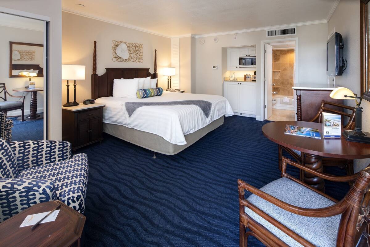 A hotel room with a large bed, a desk, a chair, a TV, and a bathroom visible through an open door.