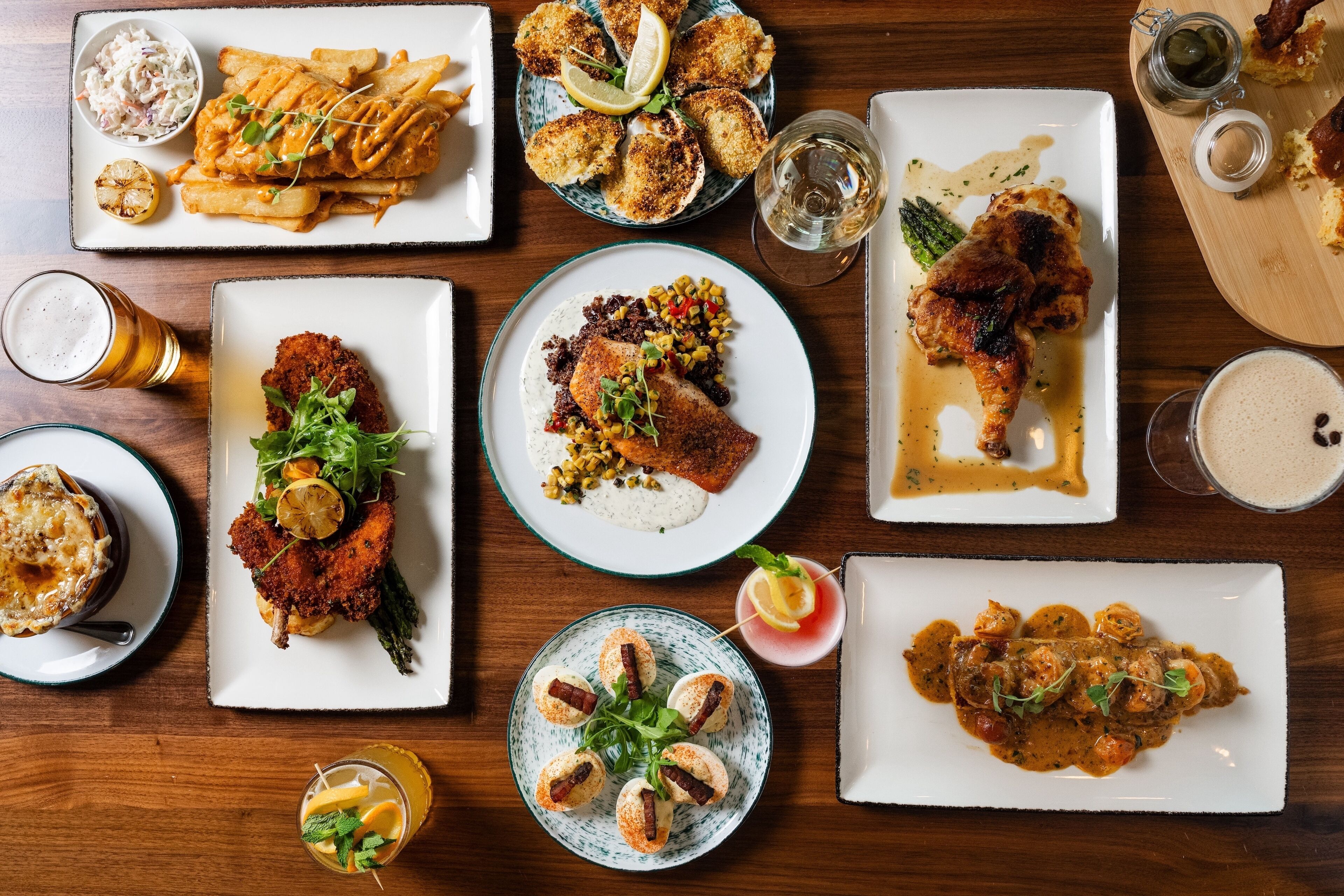 Variedad de platos sobre una mesa de madera, como pescado con papas fritas, un bistec y un plato de pollo.
