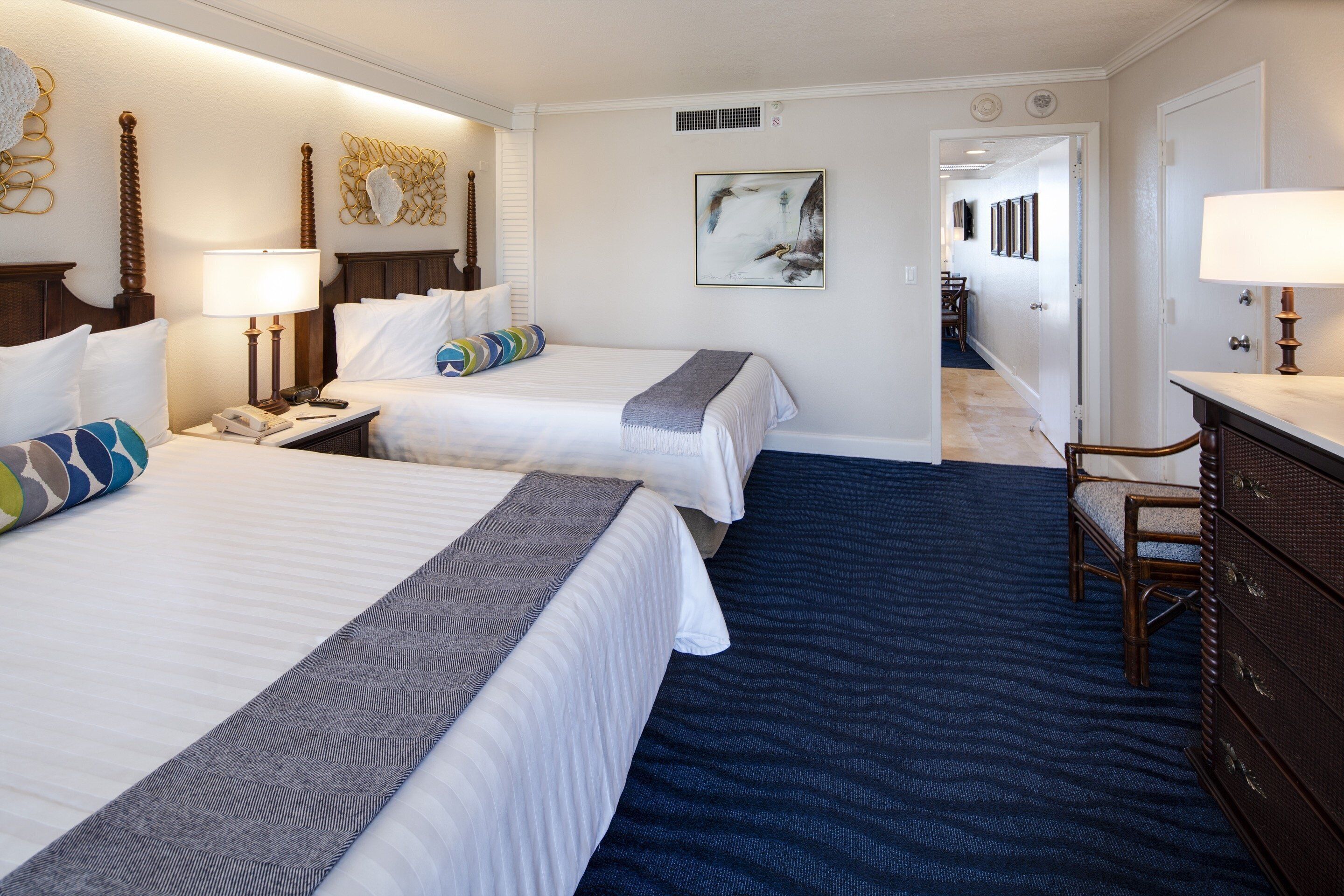 Habitación de hotel con dos camas, un escritorio, un tocador y un baño visible a través de una puerta abierta.