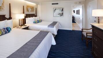 Habitación de hotel con dos camas, un escritorio, un tocador y un baño visible a través de una puerta abierta.