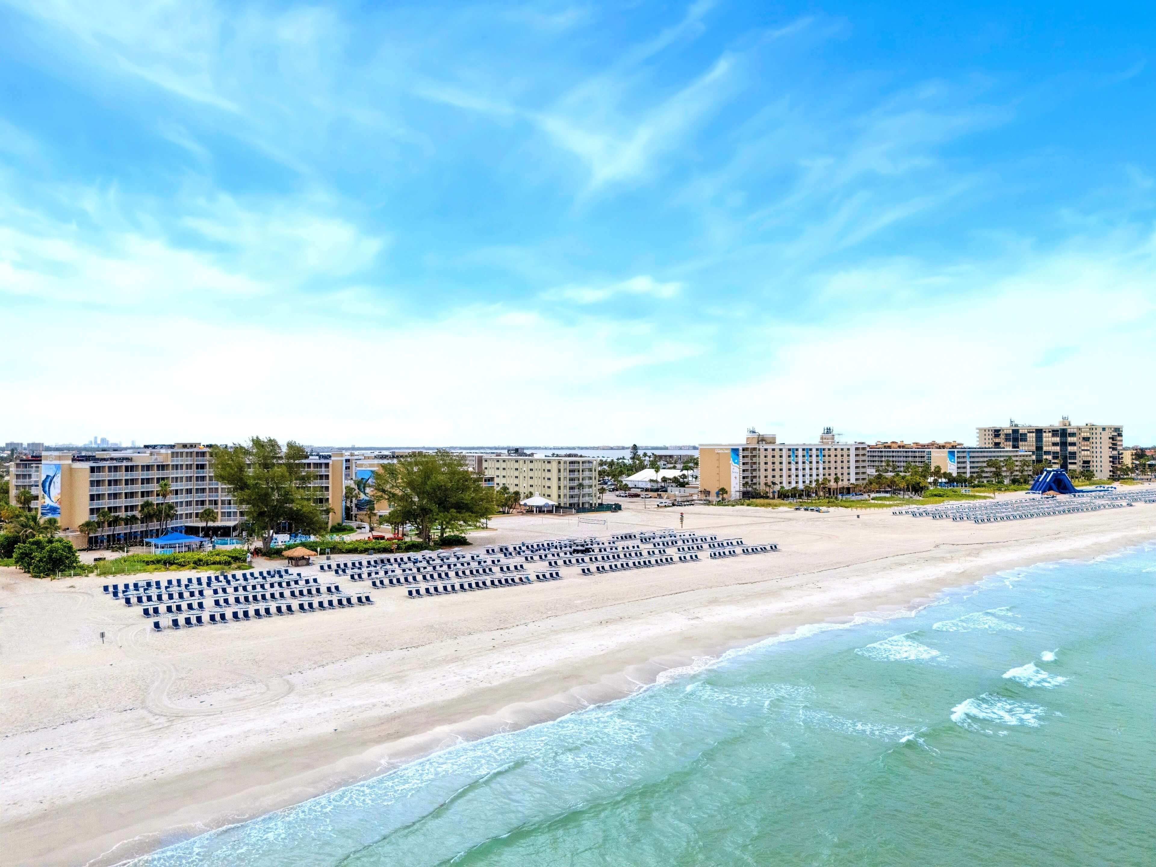 A beachside hotel with rows of sun loungers, a pool area, and a view of the ocean.