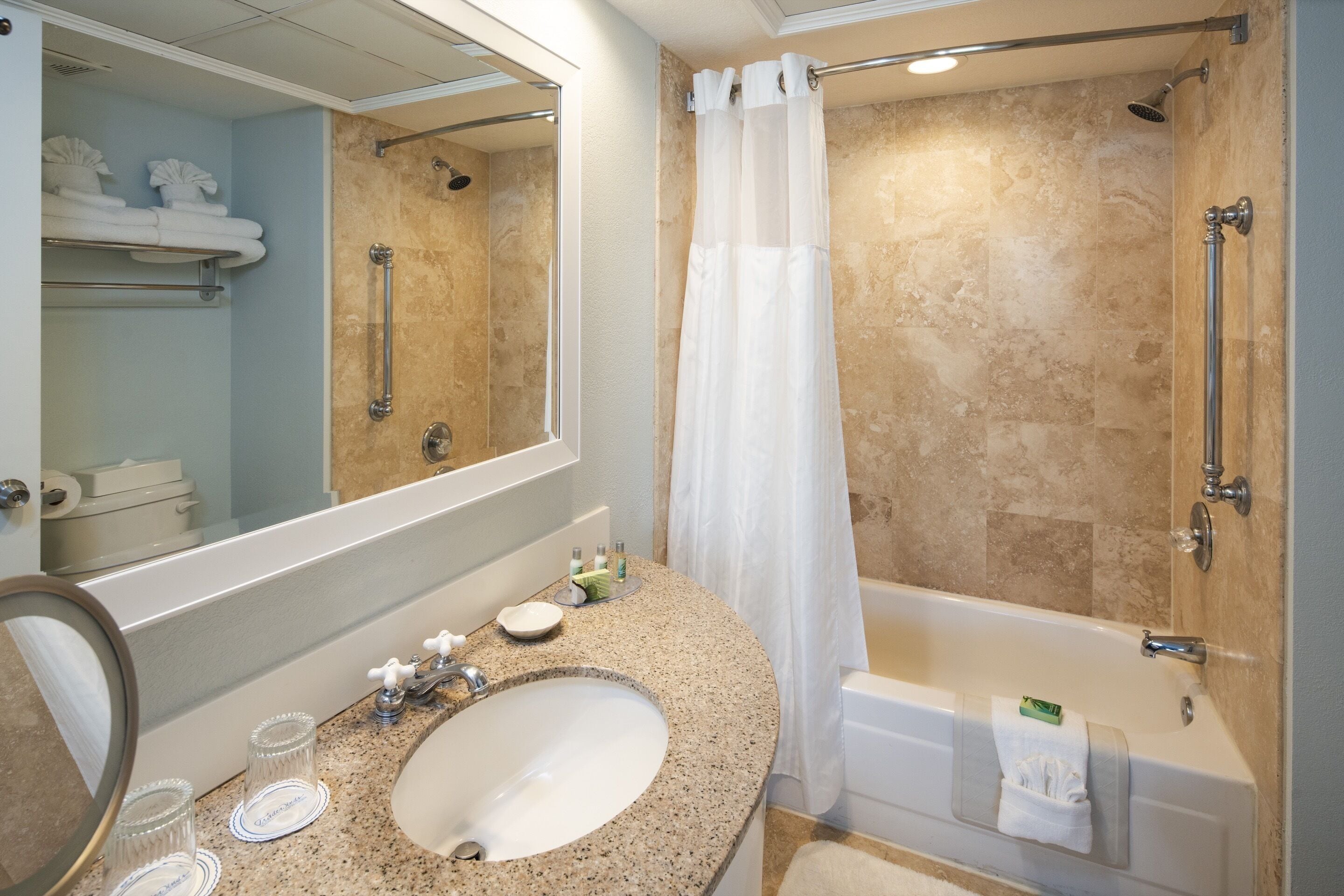 Un baño con lavamanos de granito, un espejo grande, una bañera y una ducha con cortina.