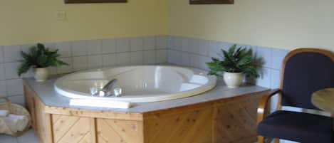 Un baño con una bañera de madera, dos plantas en macetas y cuadros en la pared.