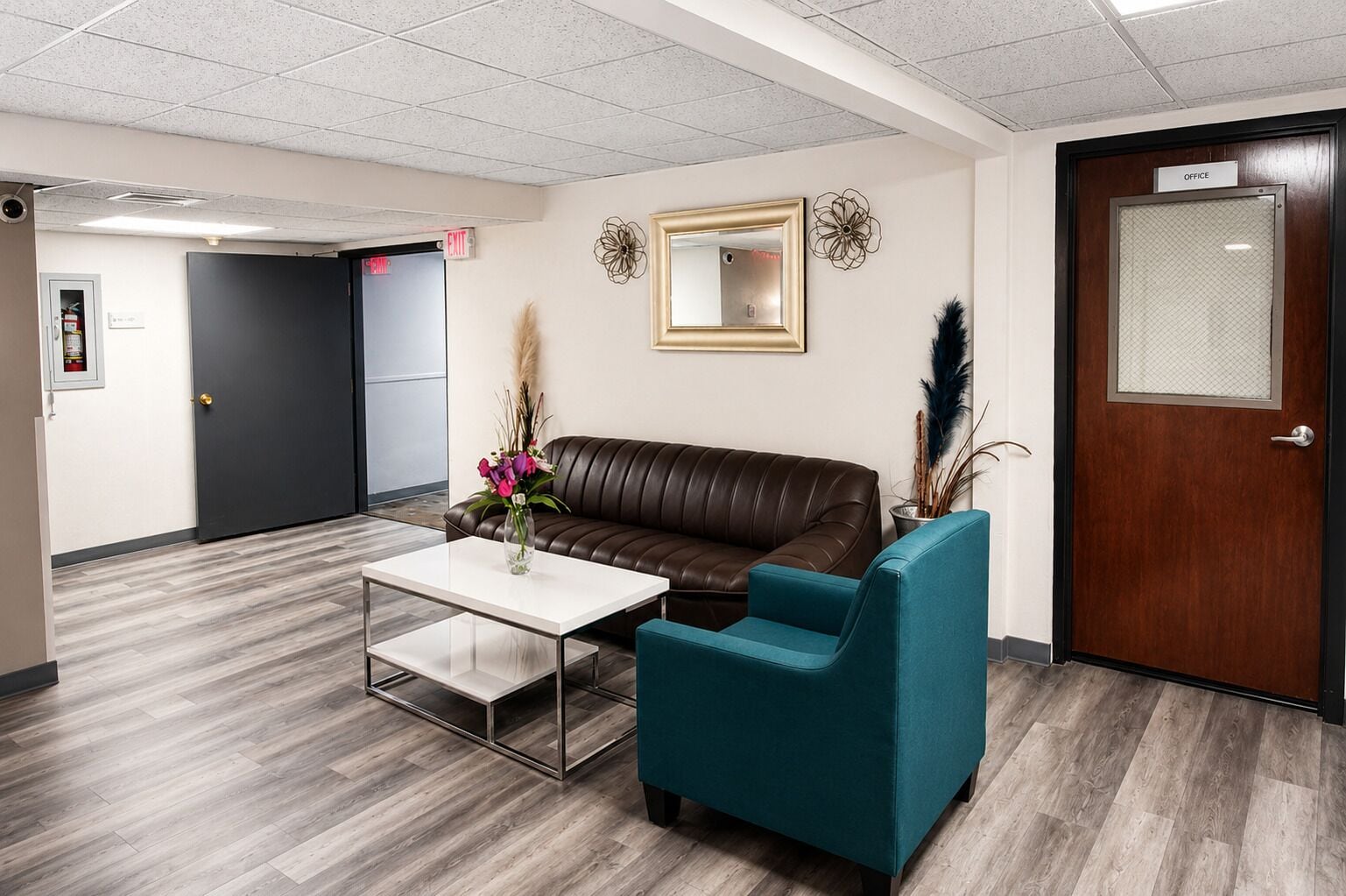 A reception area with a leather couch, teal armchair, and a white coffee table.