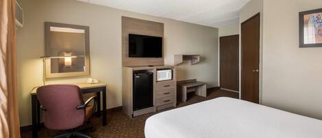 Habitación de hotel con cama, escritorio, silla, televisión y minibar.