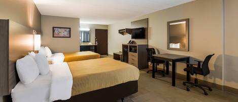A hotel room with two beds, a desk, a chair, a TV, and a bathroom.
