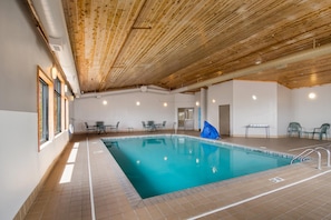 A swimming pool with a wooden ceiling and tiled floor, surrounded by tables and chairs. - Econo Lodge Duluth near Miller Hill Mall (Duluth)