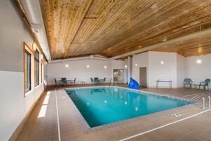 Una piscina con techo de madera y suelo de baldosas, rodeada de mesas y sillas.