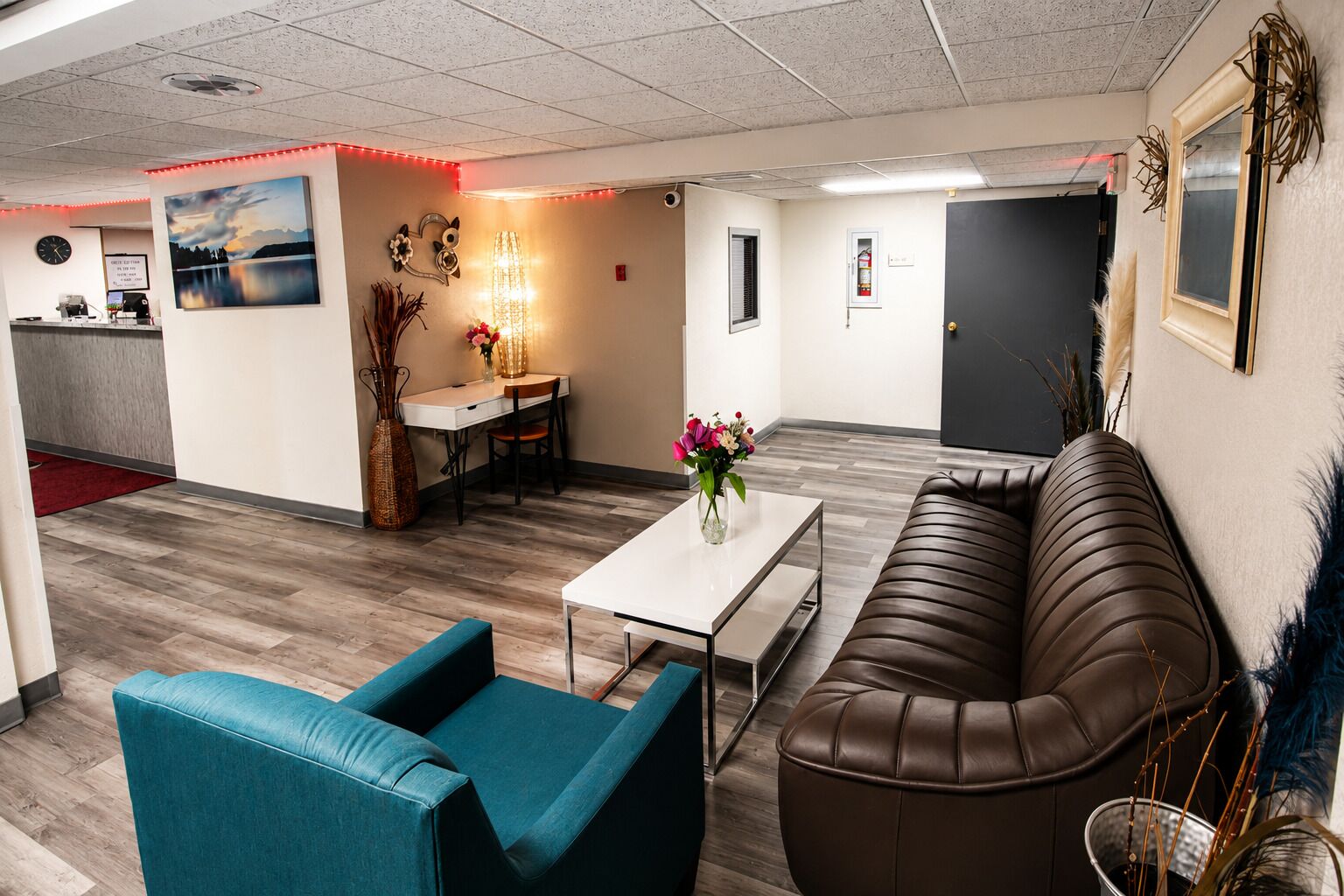 Un hall de hotel con recepción, zona de comedor, un sofá y una mesa baja con flores.