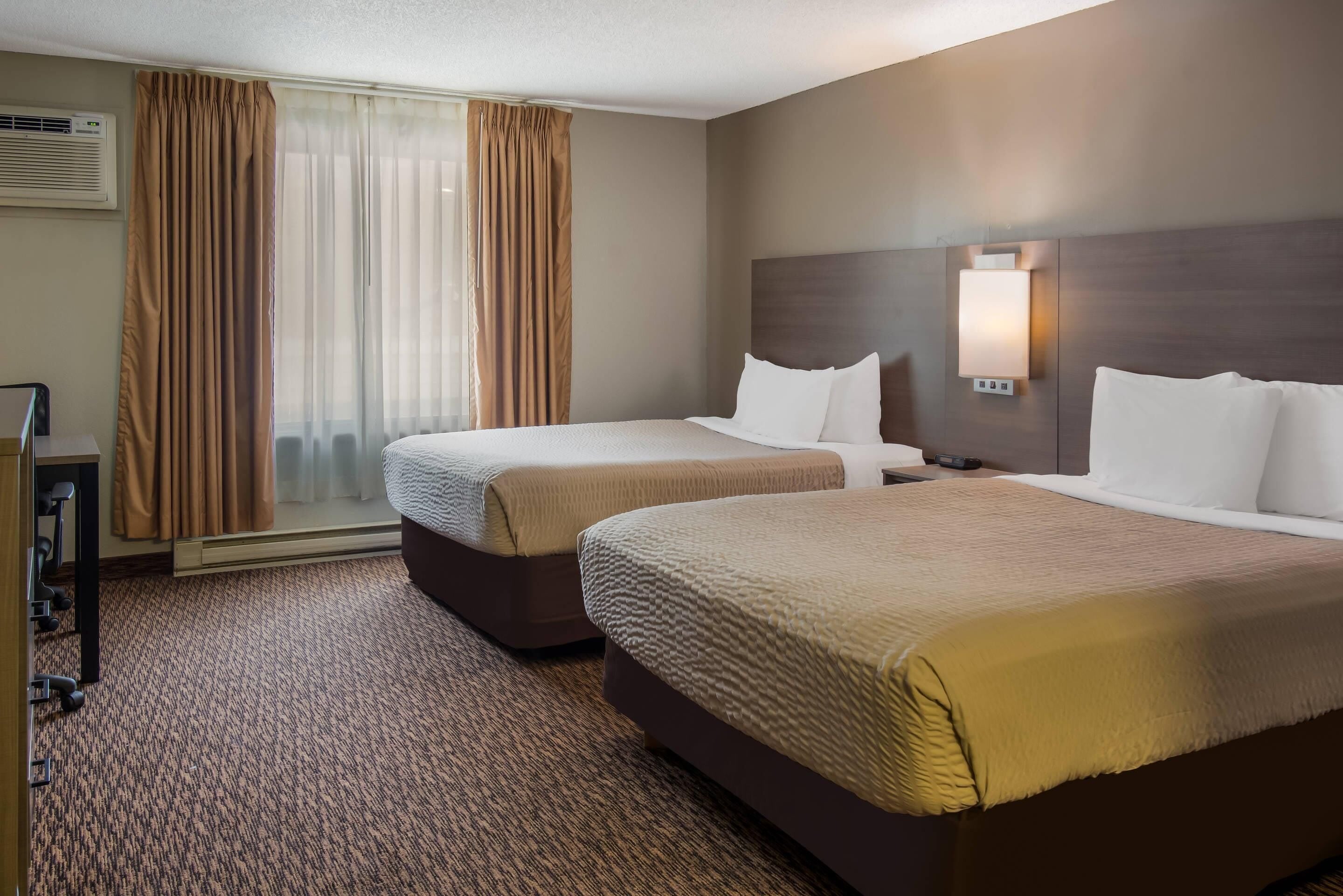 A hotel room with two beds, a desk, and a window with curtains.
