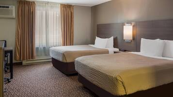 A hotel room with two beds, a desk, and a window with curtains.