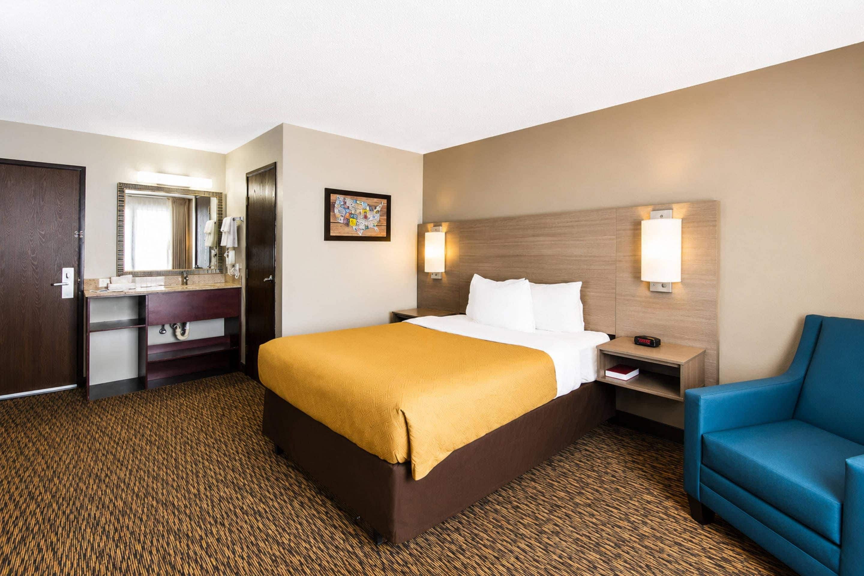 A hotel room with a bed, a desk with a chair, a bathroom, and a wall-mounted lamp.