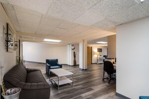 Un amplio espacio de oficina con sofá, mesa de centro, escritorio con computadora y mostrador de recepción con un letrero.