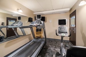 Un gimnasio con cintas de correr, una televisión instalada en la pared, un reloj y una puerta.