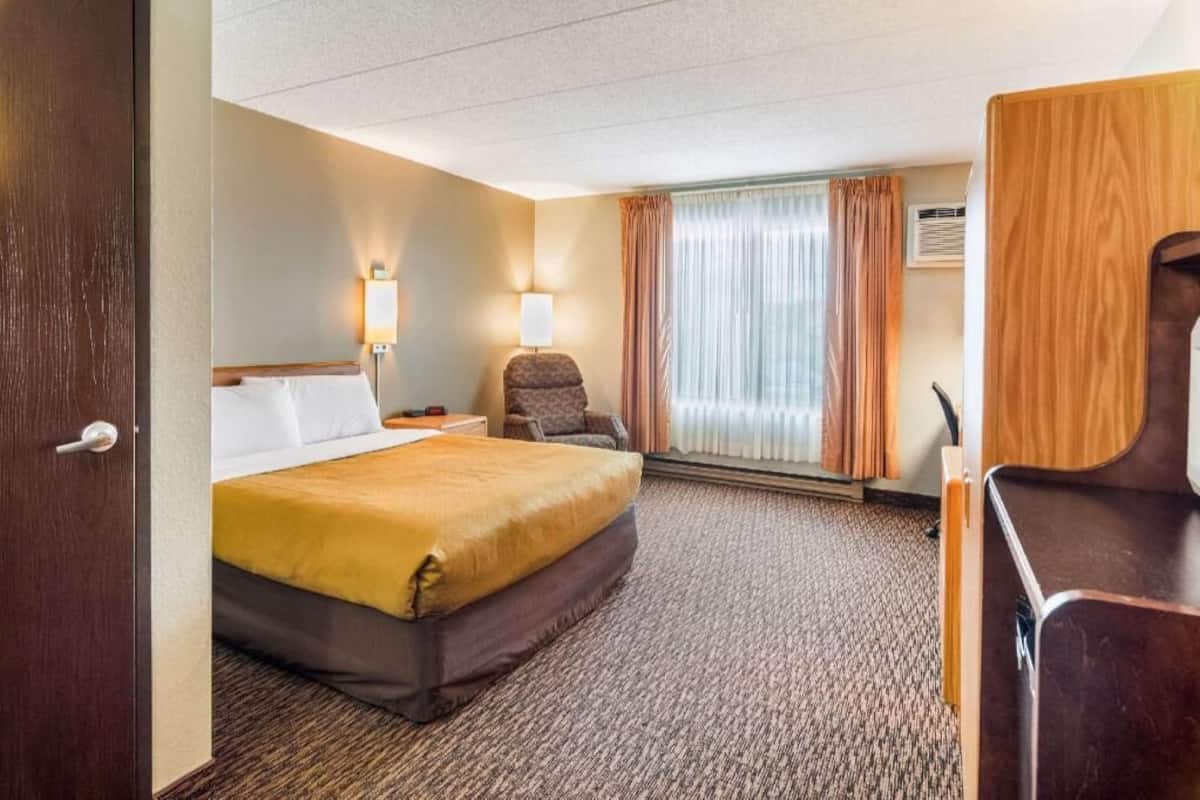 A hotel room with a bed, a desk, a chair, a lamp, and a window with curtains.