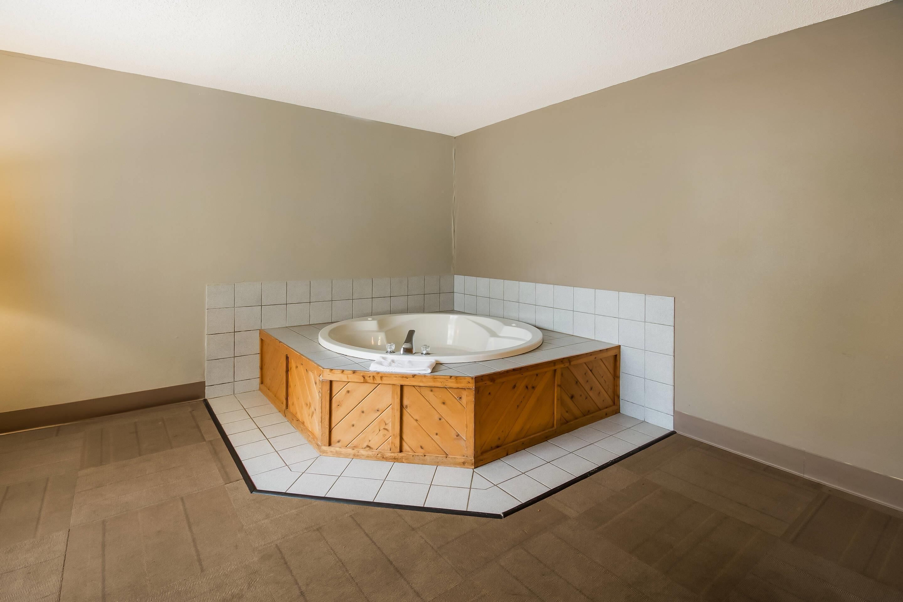 A corner bathroom with a freestanding bathtub, tiled walls, and a wooden floor.
