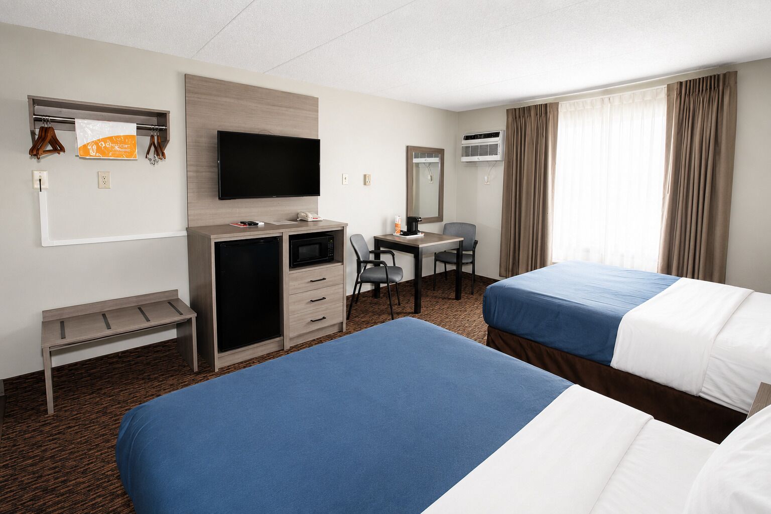 Une chambre d’hôtel avec deux lits, un bureau avec une chaise, une télévision, un minibar et un appareil de climatisation.