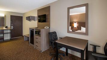 A hotel room with a desk, chair, minibar, and a television mounted on the wall.