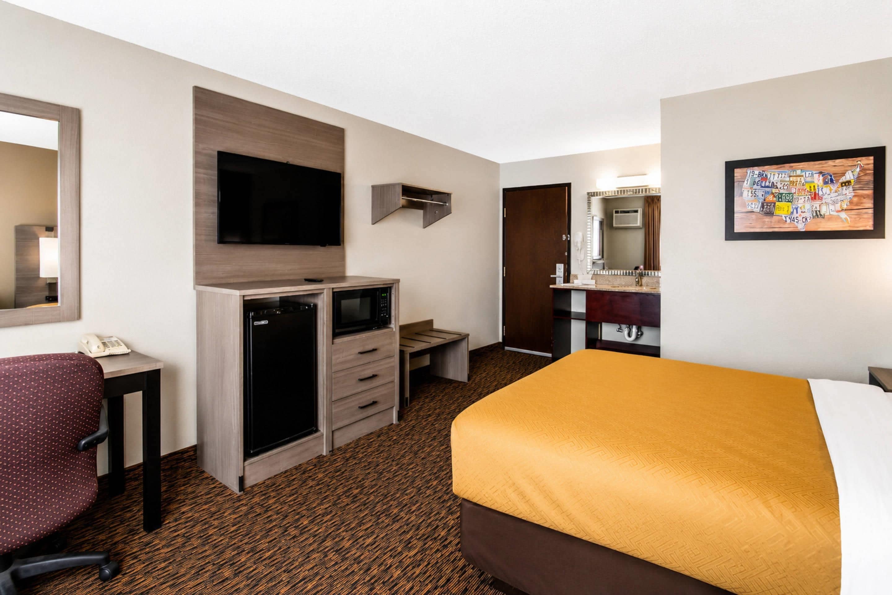 Une chambre d’hôtel comprenant un lit, un bureau avec un ordinateur, un four à micro-ondes, une chaise, un téléviseur et une salle de bain avec un miroir et un lavabo.
