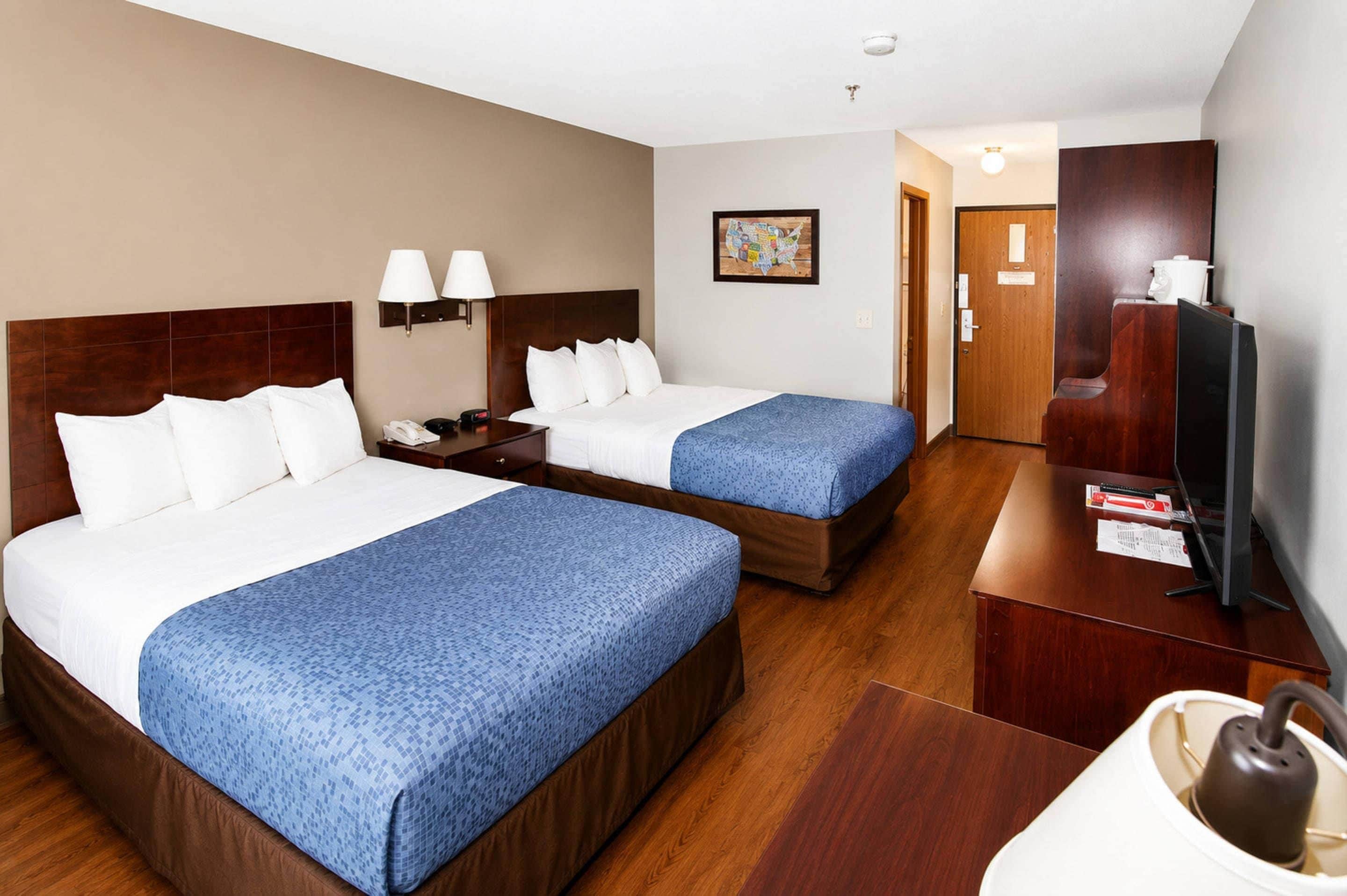 A hotel room with two beds, a desk, a television, and a coffee machine.