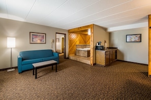 A hotel room with a blue sofa, a small table, a wooden cabinet, and a painting on the wall. - Econo Lodge Duluth near Miller Hill Mall (Duluth)