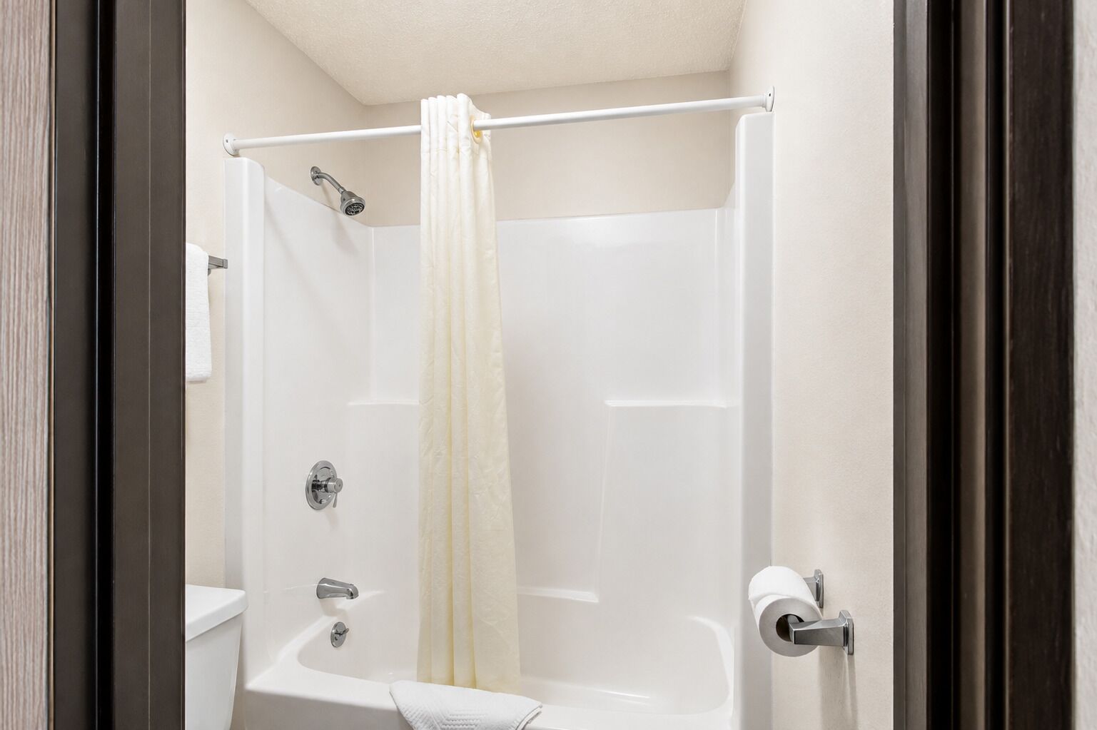 Un espace douche doté d’un rideau blanc, d’un pommeau de douche à main et d’un porte-rouleau de papier toilette.