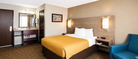 A hotel room with a bed, a desk, a chair, a mirror, and a wall-mounted lamp.