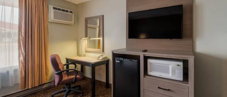 A hotel room with a desk, chair, television, microwave, and a minibar.