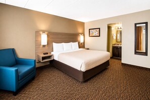A hotel room with a bed, a nightstand, a blue armchair, a wall-mounted lamp, a painting, a mirror, and a bathroom door. - Econo Lodge Duluth near Miller Hill Mall (Duluth)