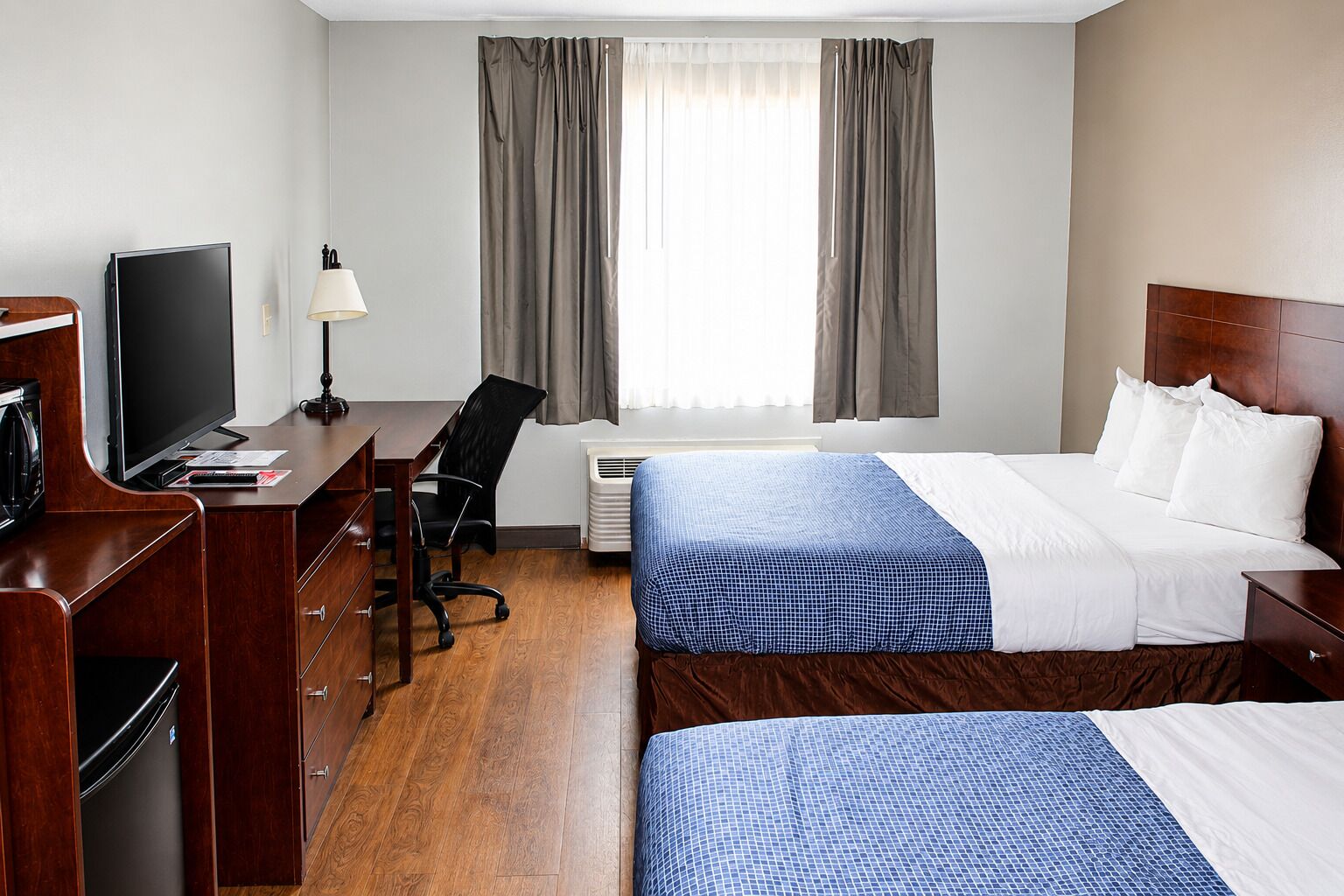 Een hotelkamer met een bed, een bureau met stoel, een televisie en een raam met gordijnen.