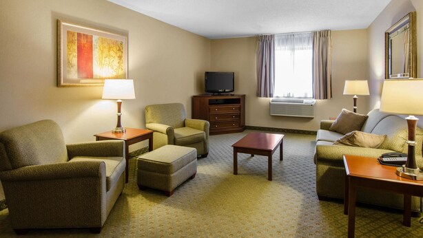 A hotel room with a sofa, armchair, ottoman, a flat-screen TV, a small table, and a lamp.