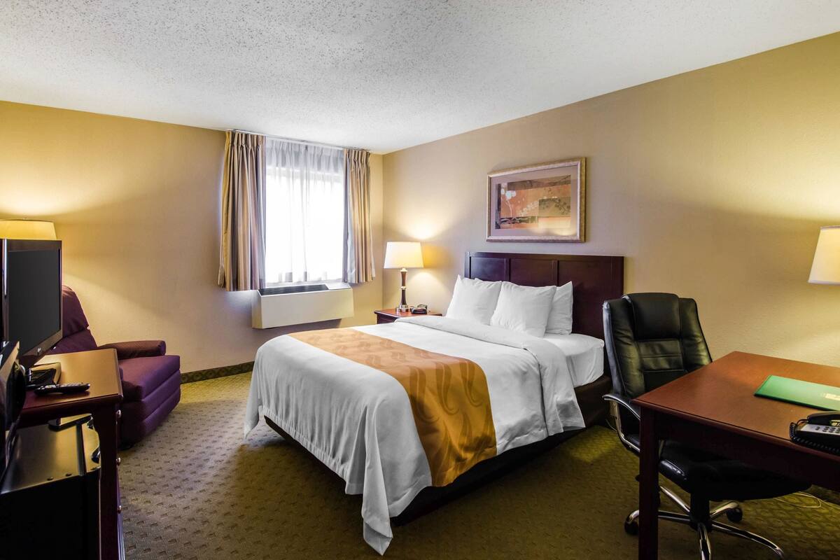 A hotel room with a large bed, a desk, a chair, a television, and a window with curtains.