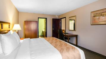 Una habitación de hotel con una cama, un escritorio, una silla, una lámpara y una puerta.