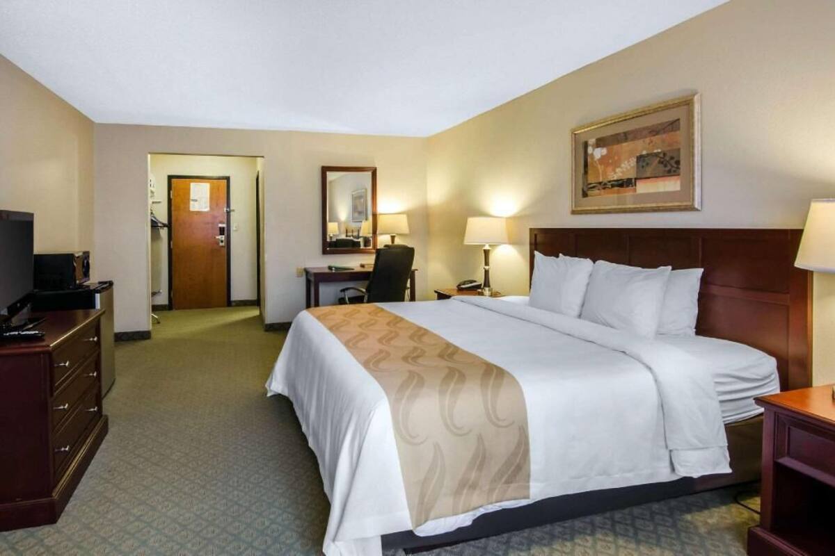 A hotel room with a bed, a desk, a chair, a TV, and a painting on the wall.