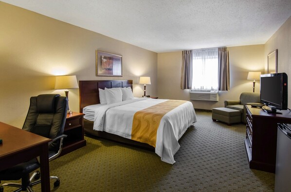 A hotel room with a bed, desk, chair, television, and a window with curtains.