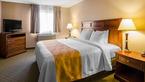 A hotel room with a bed, bedside lamps, a TV, a dresser, and a window with curtains.