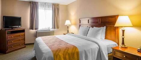 A hotel room with a bed, bedside lamps, a TV, a dresser, and a window with curtains.