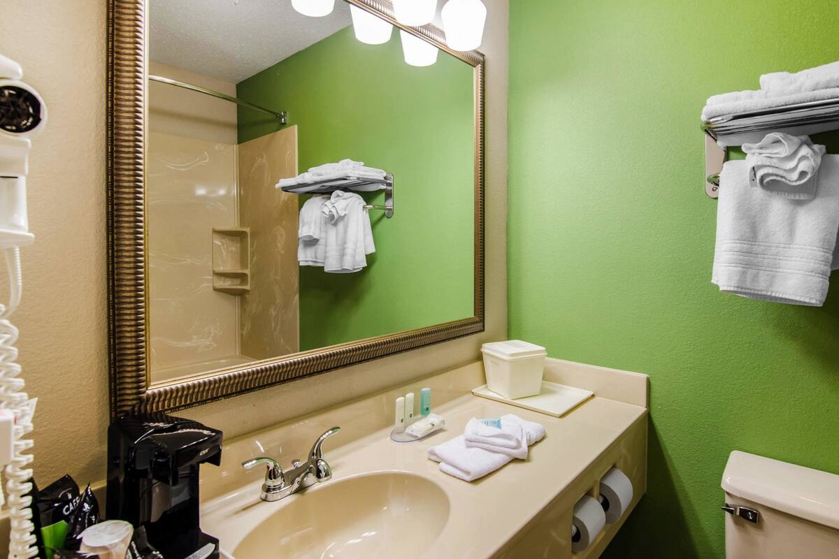 A bathroom with a beige sink, a large mirror, green walls, and white towels.